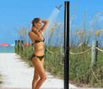 mujer duchándose en una ducha solar negra junto a la playa