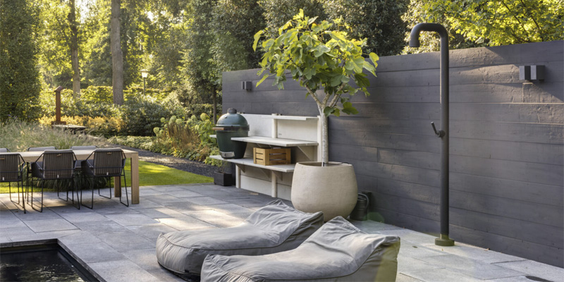 Ducha exterior JEE-O Soho, de color negro, en un jardín con piscina